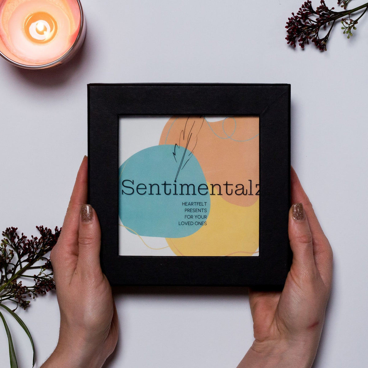 Geschenkbox mit Fenster für das Kartenset zum Ausfüllen, von zwei Händen gehalten, mit Kerze und Blüten, Sentimentalz